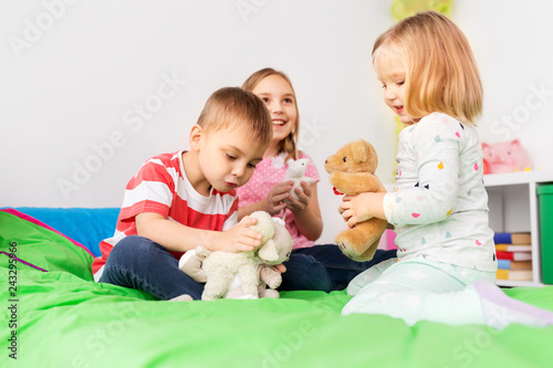 childhood, leisure and people concept - happy children playing with soft toys at home