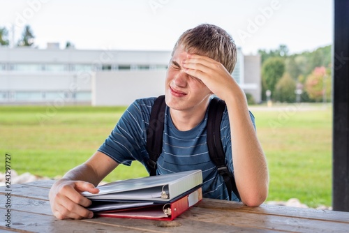 Bored teenager reluctant to do his homework while sitting at an outdoor table.