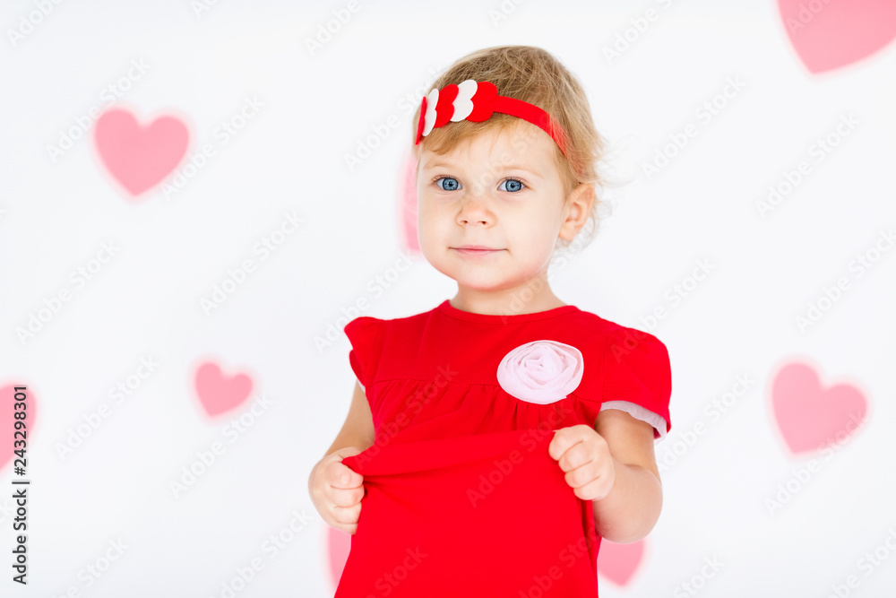 Little blonde girl in red dress with red wreath with heatrs on the white background with pink hearts on the St. Valentine's day