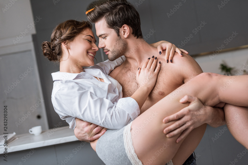 passionate man holding in arms smiling girlfriend at home - obrazy, fototapety, plakaty 