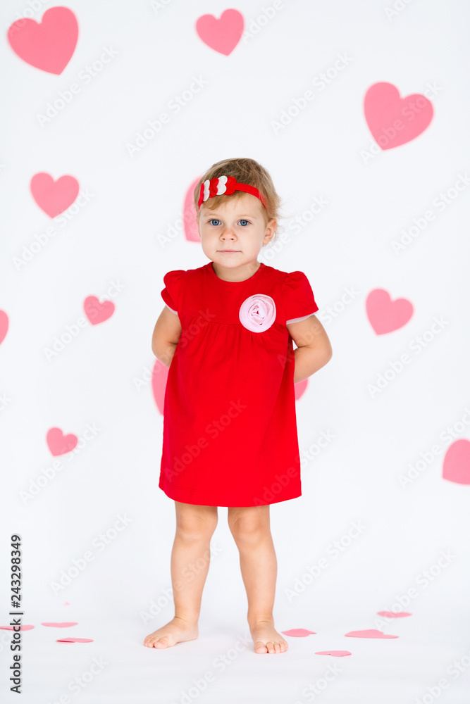 Little blonde girl in red dress with red wreath with heatrs on the white background with pink hearts on the St. Valentine's day