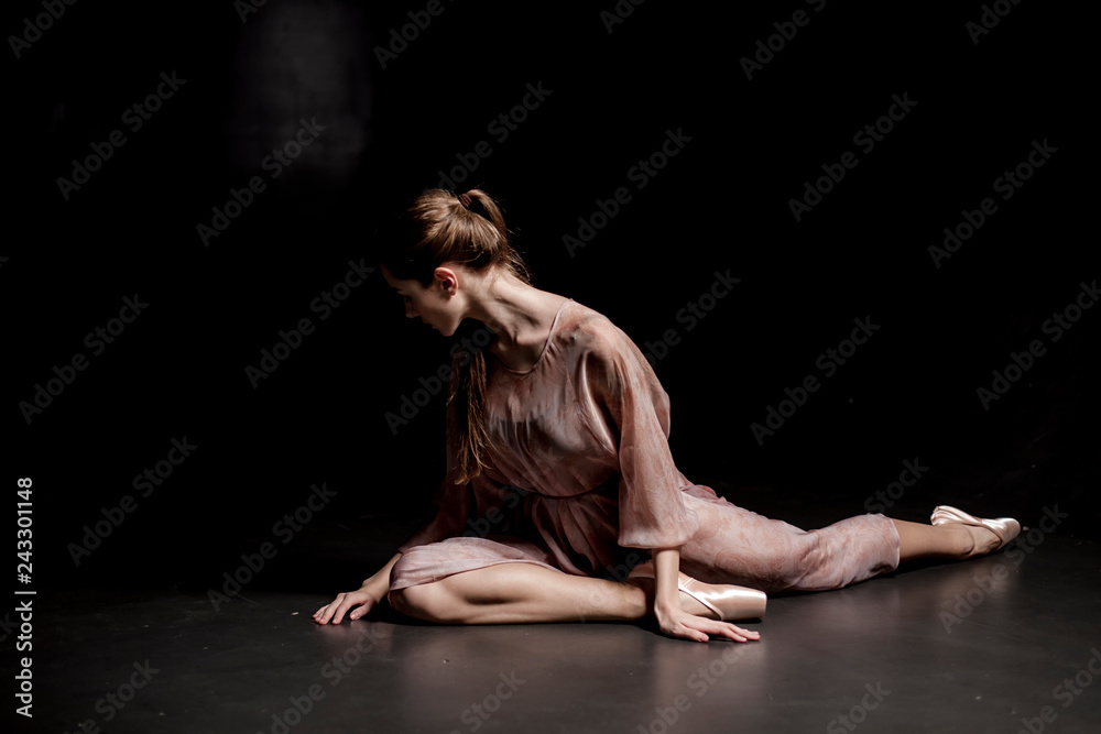 Tired ballerina sitting on stage on black background close up
