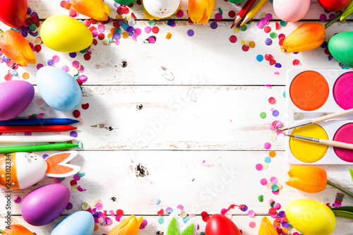 Easter background with eggs, tulips and confetti on white wooden background. Top view. Copyspace