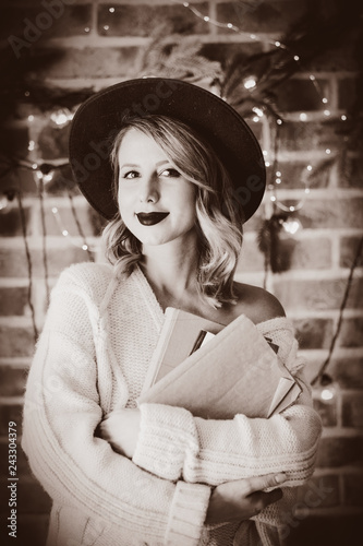 Portrait of a young cozy woman in white sweater with books and Christmas lights and pine branch on background. photo