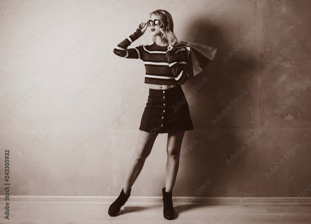Portrait of a young style blonde girl in red striped sweater with shopping bags on grey background. Portrait of a young style blonde girl in red striped sweater with shopping bags on grey background.