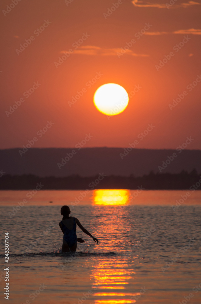 Children swim in the river at sunset.