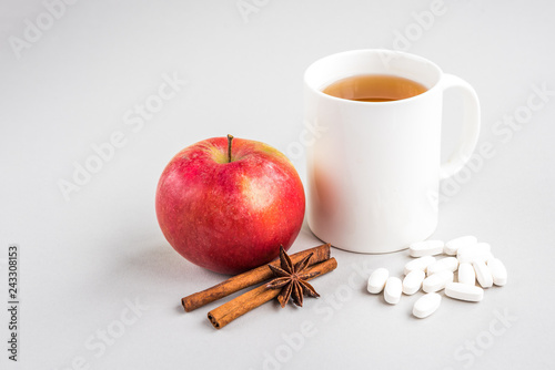 Mug of hot tea with apple and cinnamon and pills on gray background. Season flu. Disease.