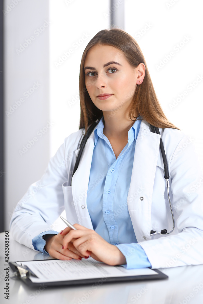 Doctor woman filling up medical form while sitting at the desk in hospital office. Physician at work. Medicine and health care concept Doctor woman filling up medical form while sitting at the desk in hospital office. Physician at work. Medicine and health care concept