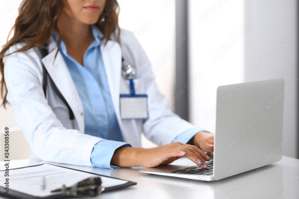 Unknown doctor woman typing on laptop computer while sitting at the desk in hospital office. close-up of hands. Physician at work. Medicine and health care concept Unknown doctor woman typing on laptop computer while sitting at the desk in hospital office. close-up of hands. Physician at work. Medicine and health care concept