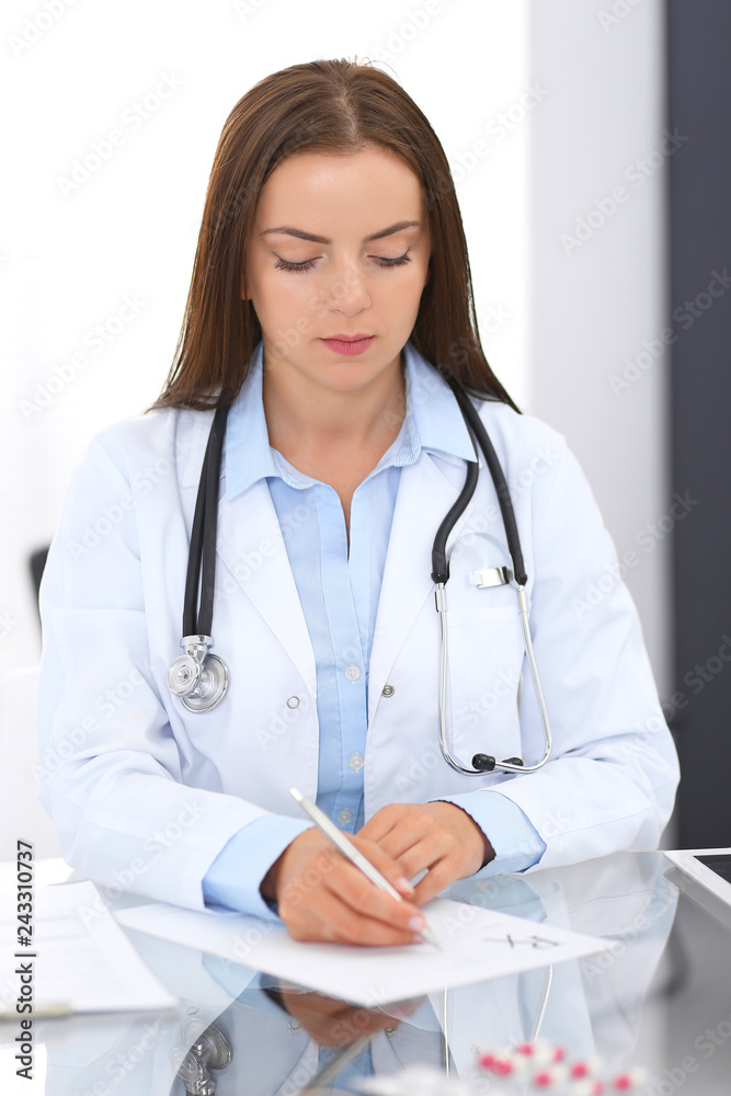Doctor woman at work. Portrait of female physician filling up medical form while sitting at the glass desk at clinic or hospital. Medicine and healthcare concept Doctor woman at work. Portrait of female physician filling up medical form while sitting at the glass desk at clinic or hospital. Medicine and healthcare concept