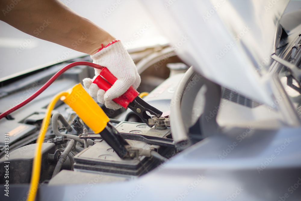 Car mechanic man using battery jumper cables to charge a dead battery..Close up hand charging