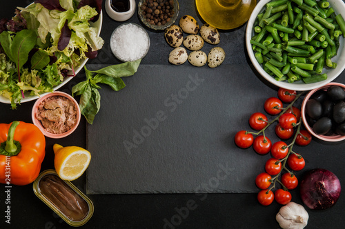 Fototapeta Naklejka Na Ścianę i Meble -  Top view. Ingredients for making French traditional niçoise (nicoise) salad around a black stone cutting board. Copy space.
