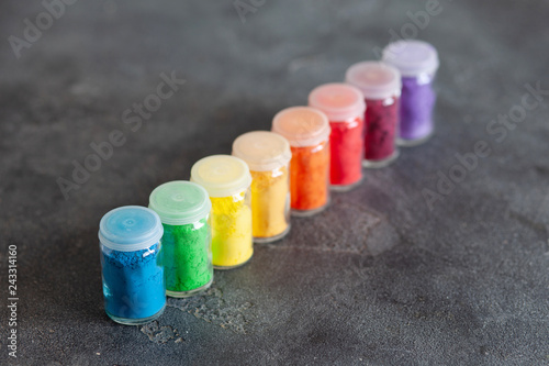 Bright colourful powdered pigments in glass bottles for Indian holi festival on dark slate background, copy space