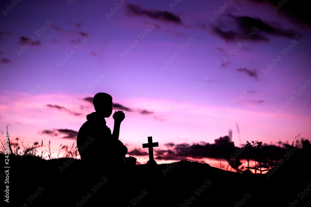 Boy sitting and praying with light of sunset , christian silhouette concept.