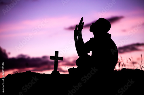 Boy sitting and praying with cross, christian silhouette concept.