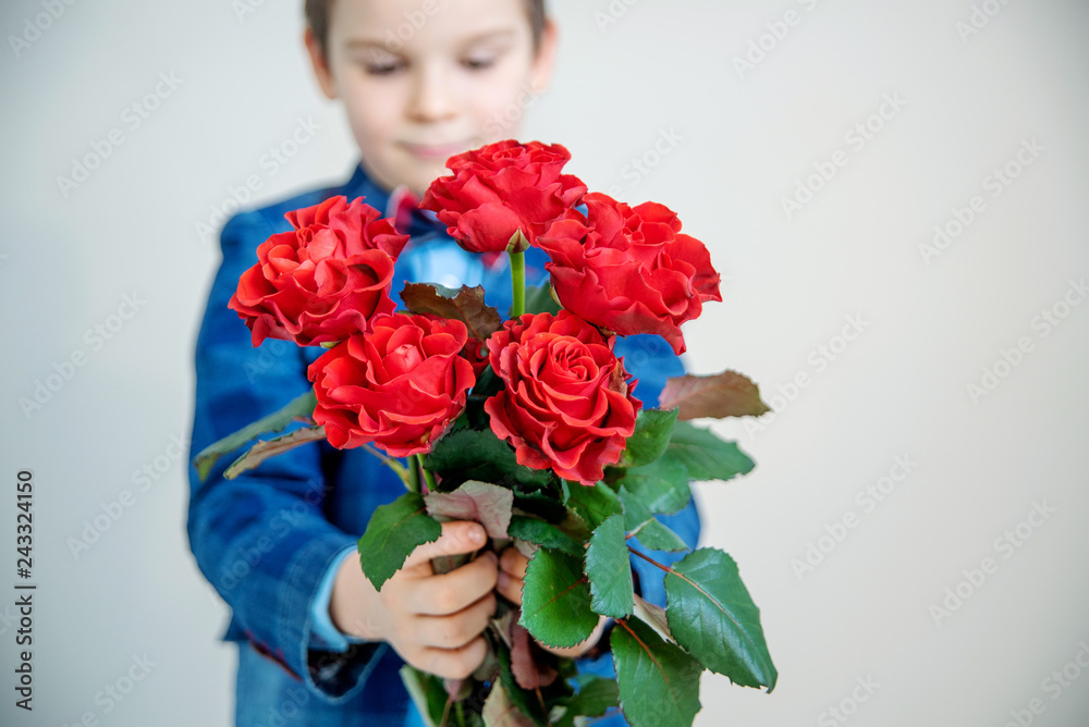 Adorable little boy in suit with bouquet of red roses on a light background Adorable little boy in suit with bouquet of red roses on a light background