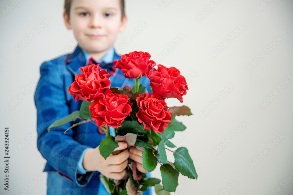 Adorable little boy in suit with bouquet of red roses on a light background Adorable little boy in suit with bouquet of red roses on a light background