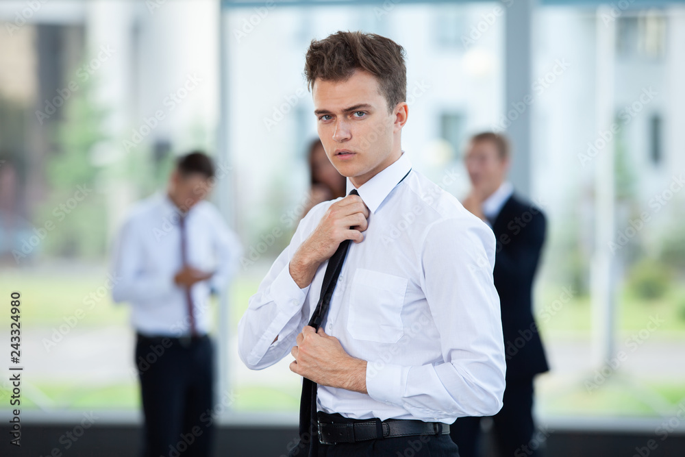 Smiling Businessman posing while colleagues talking together in office. Smiling Businessman posing while colleagues talking together in office.