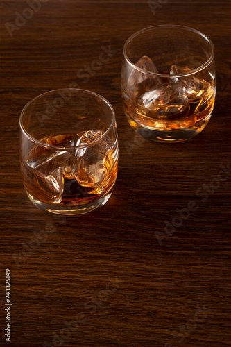 Two glasses of whiskey with ice on a wooden background