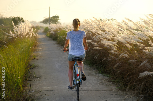 Tourist woman cycling through fields during sunset in in Hoi An, Vietnam.