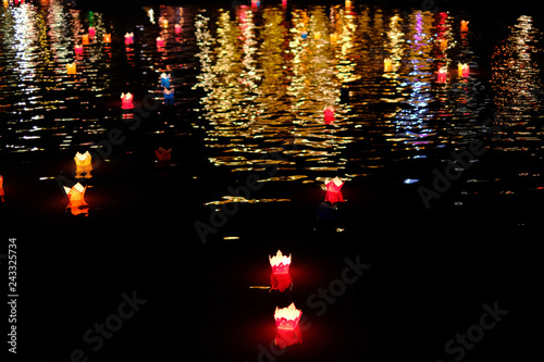 Candle lanterns floating on a river among colorful reflections during night in Hoi An, Vietnam.