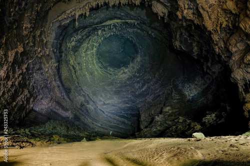 Man with headlight standing on a rock under a high wall with stalactites inside the giant Hang Tien cave in the Phong Nha Ke national park in Vietnam.