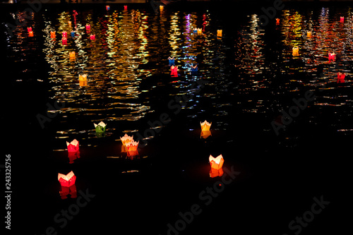 Candle lanterns floating on a river among colorful reflections during night in Hoi An, Vietnam.