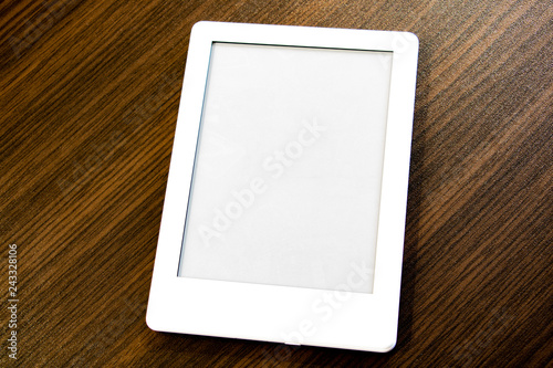 A portable e-book with two clipping paths for the book and screen lies on the table. You can add your own text or image.