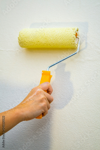 woman hand holding a yellow roller on bright wall background