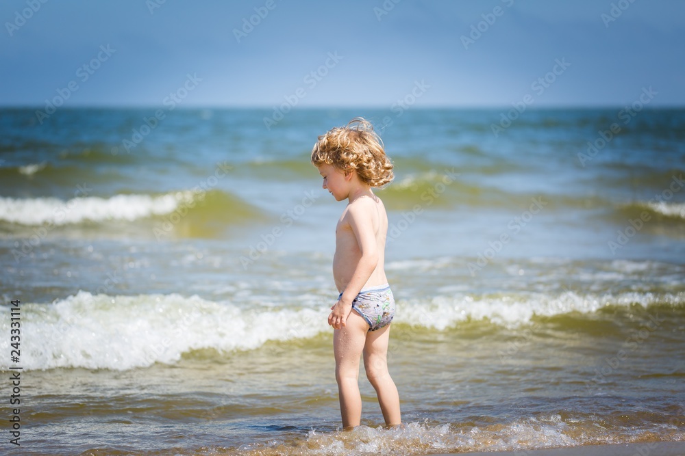 Young caucasian boy playing on sea shore at sunny summer