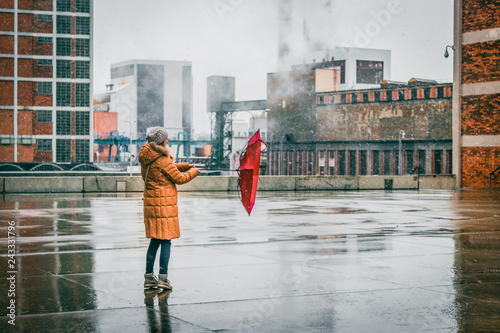 Woman with red umbrella is walking in idustrial city during blizzard photo