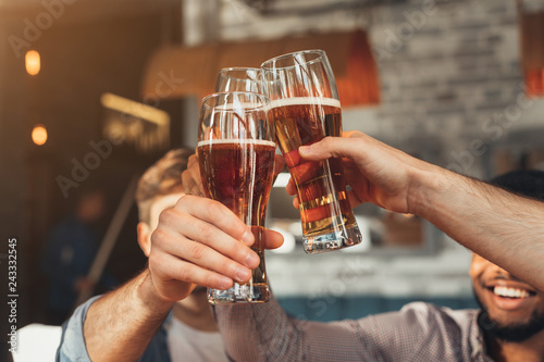 Male friends clinking beer glasses in bar  closeup