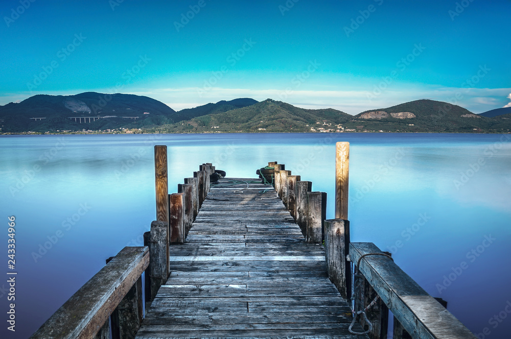 Wooden pier or jetty on a blue lake sunset and sky reflection on water. Versilia Tuscany, Italy