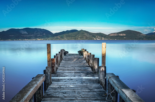 Wooden pier or jetty on a blue lake sunset and sky reflection on water. Versilia Tuscany, Italy © stevanzz
