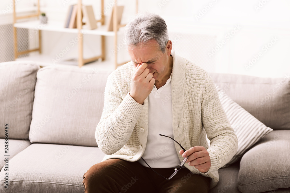 Senior man feeling tired, touching eyes at home