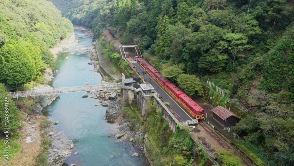 Aerial drone view over Hozu river and Sagano Sightseeing Railway or Sagano Romantic Train in Arashiyama Kyoto Japan. Sagano Romantic Train passes a gorge offering a scenic view along the Hozu River.