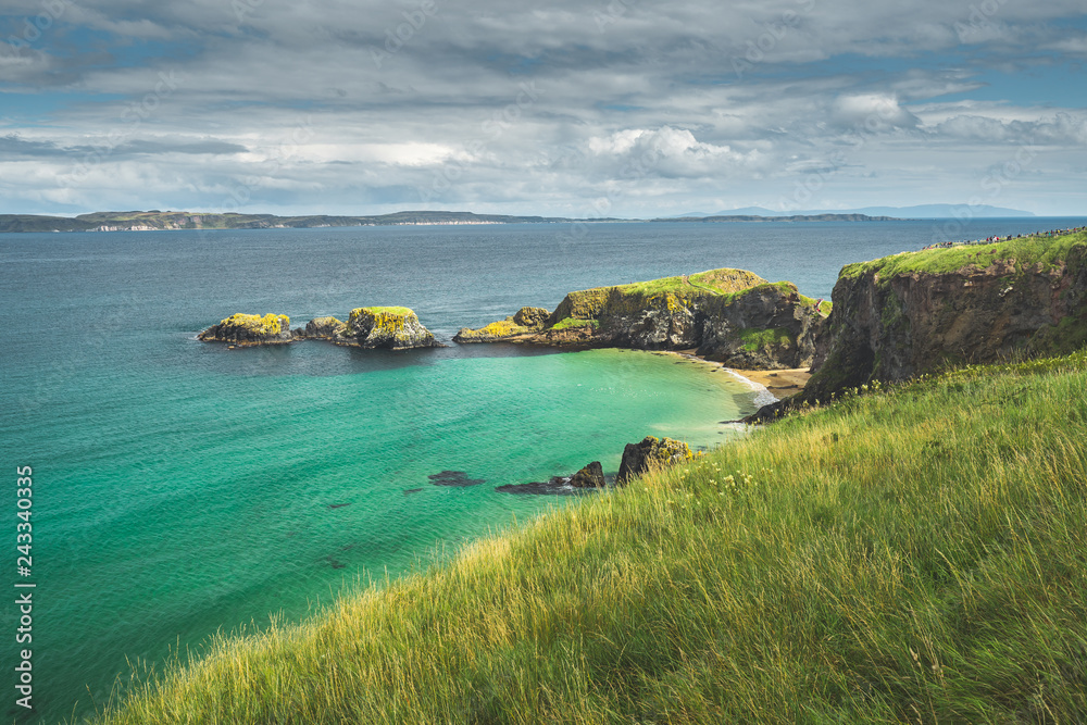 Irish bay with turquoise water and grass covered land. Northern Ireland. Breathtaking marine landscape. Grass covered land of the stunning shoreline. Beauty of wild untouched nature.
