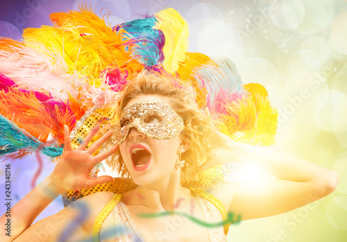 Beautiful surprised woman in carnival mask. Beauty model woman wearing masquerade mask at party over holiday background with magic glow. Christmas and New Year celebration. Glamour lady with perfect