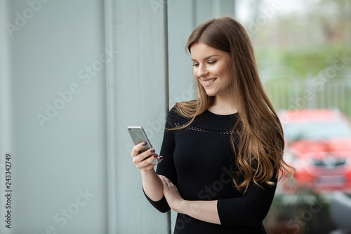Great message! Cheerful young beautiful woman using her smartphone with smile while standing at her office.