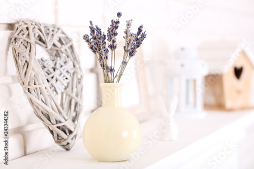 Lavender flowers in vase with decorative heart on white fireplace