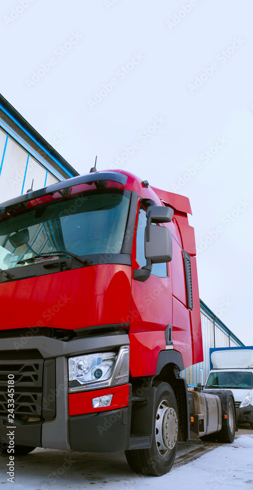 A tractor unit (prime mover or traction unit) without a semi-trailer. In the background a commercial vehicle. Front view of truck. A tractor unit (prime mover or traction unit) without a semi-trailer. In the background a commercial vehicle. Front view of truck.