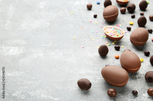 Chocolate easter eggs with colorful candies on grey wooden table