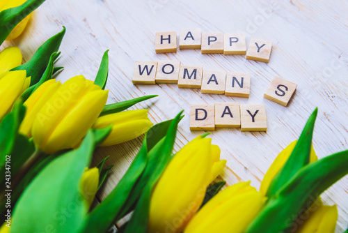 happy woman's day text. tulips overhead on white wooden background