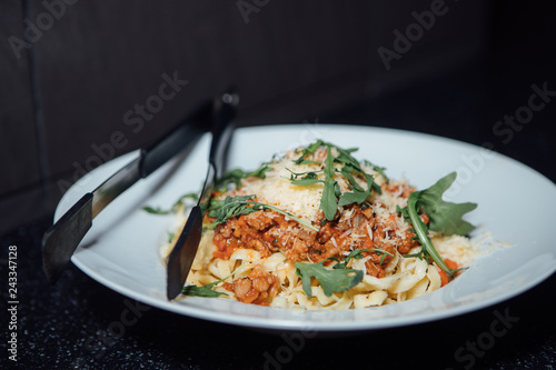 Pasta with meat and arugula sprinkled with cheese lies in a white plate