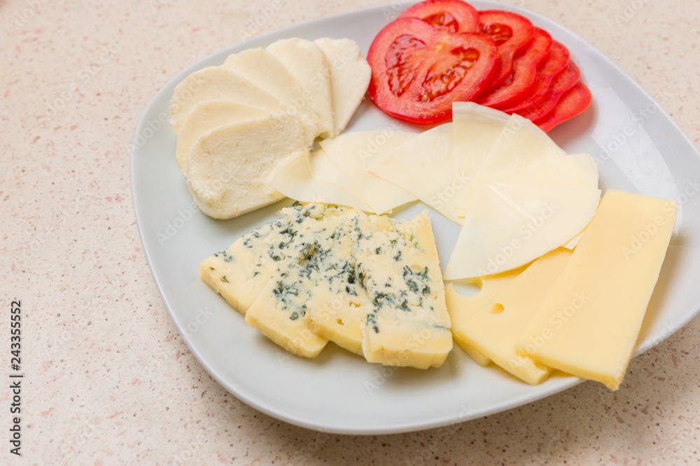 Assorted cheese sliced cheese with tomato on white plate