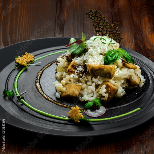 Tasty risotto cooked in a vegetable broth with porcini mushrooms and parmesan cheese on a beautiful plate. First class Italian dish on a wooden table.