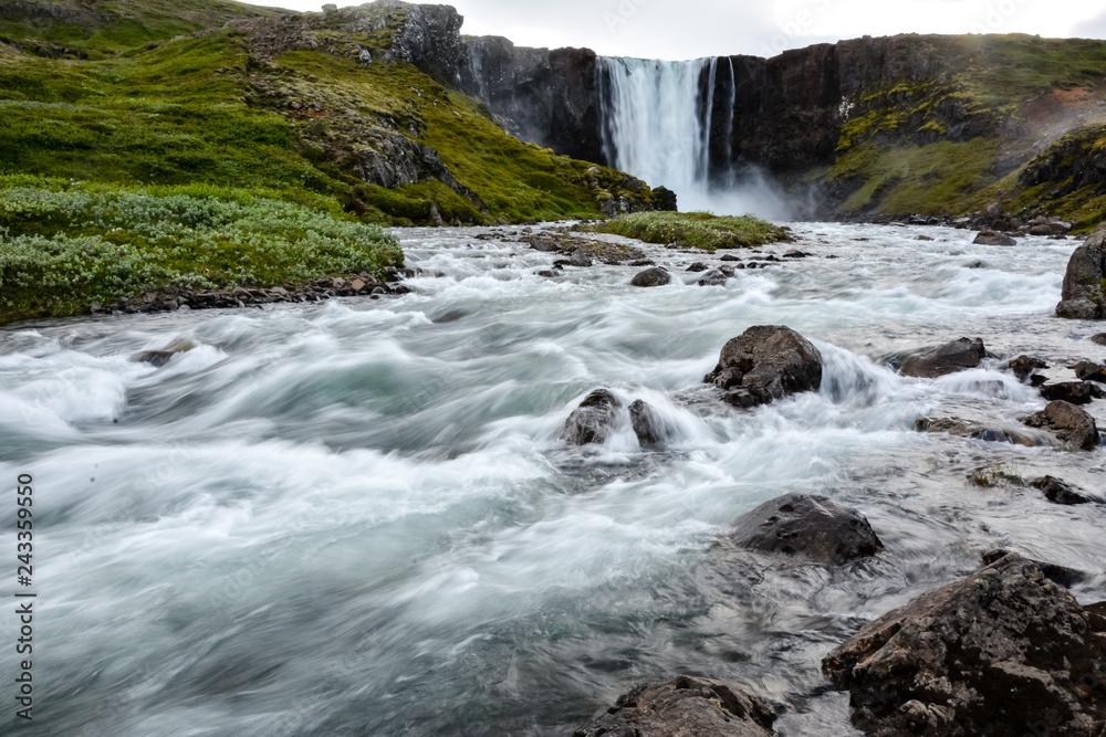 Fresh clean waterfall Gufufoss near Seydisfjordur in Iceland in  summer with loads of water flowing between rocks, snow in the background