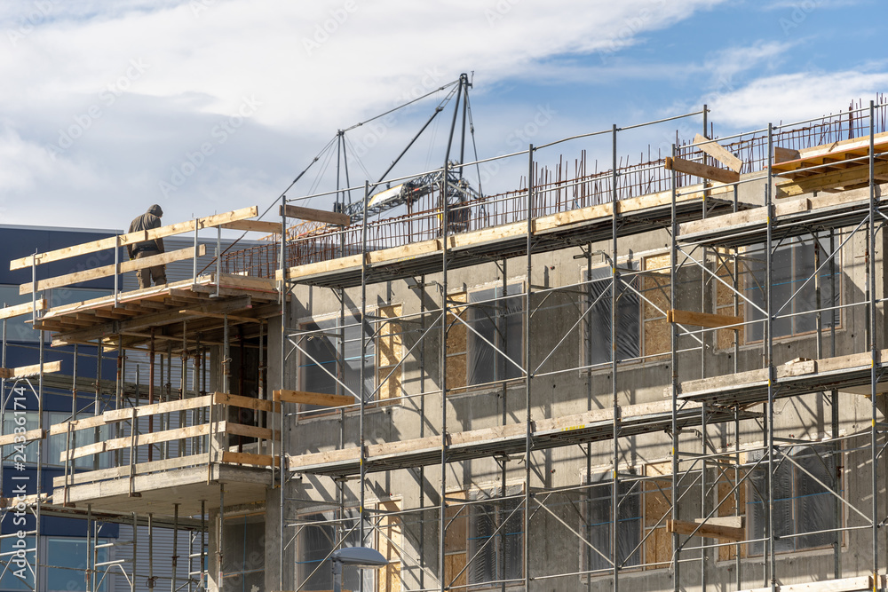 Skilled man standing on scaffolding near incomplete building Skilled man standing on scaffolding near incomplete building