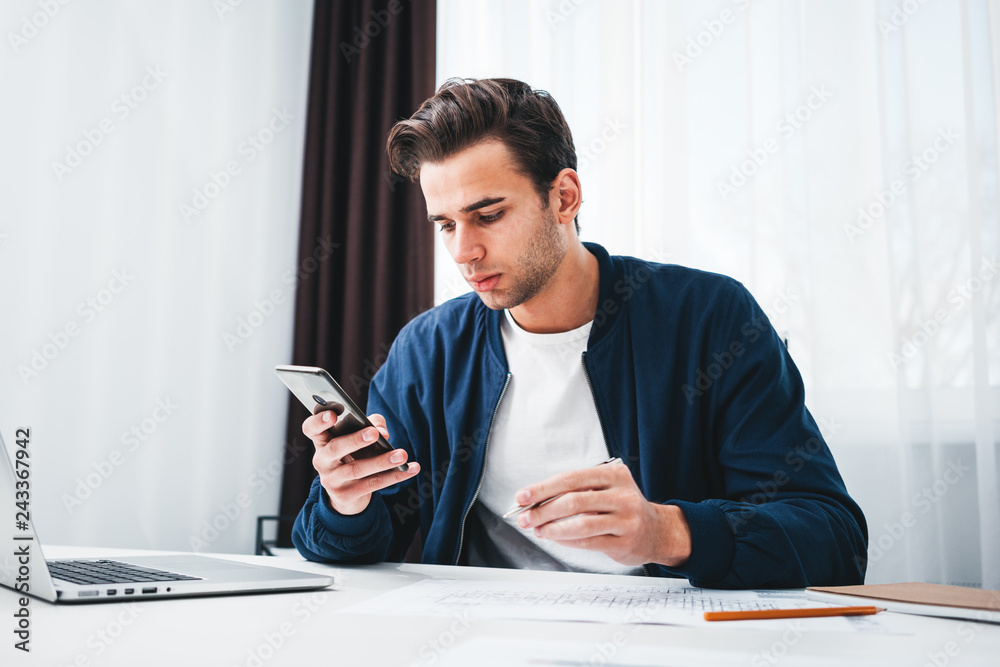 Coworker man writing in notepad and hold smartphone in hand. Concentrated student sits at her desk and preparing project