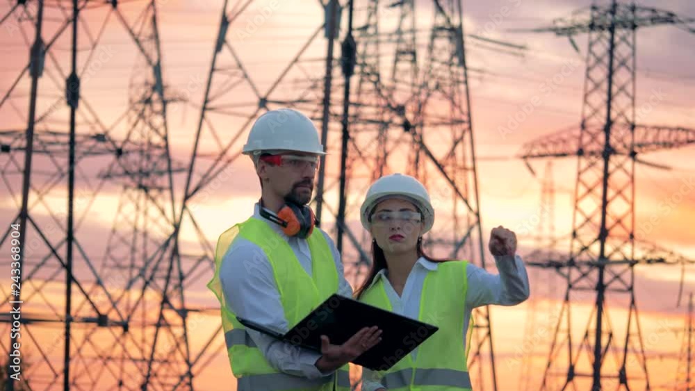 Power lines and two specialists engineers working on renewable energy development during sunset Power lines and two specialists engineers working on renewable energy development during sunset
